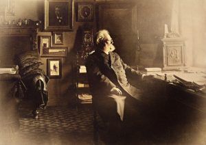 Henrik Ibsen sittende ved skrivebordet i leiligheten sin i Oslo, med lys som faller inn fra vinduet.