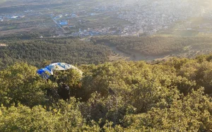 Paraglider som har landet i kratt og buskas under startområdet på Korylovos, med utsikt over byen og slettene nedenfor i ettermiddagssol.