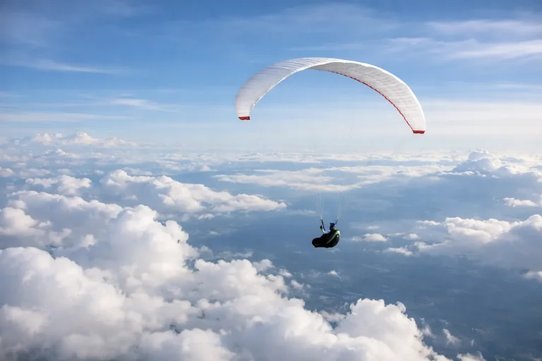 Person som flyr paraglider høyt over skyene med utsikt mot landskap langt under.