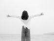 woman standing with arms stretched on beach in black and white