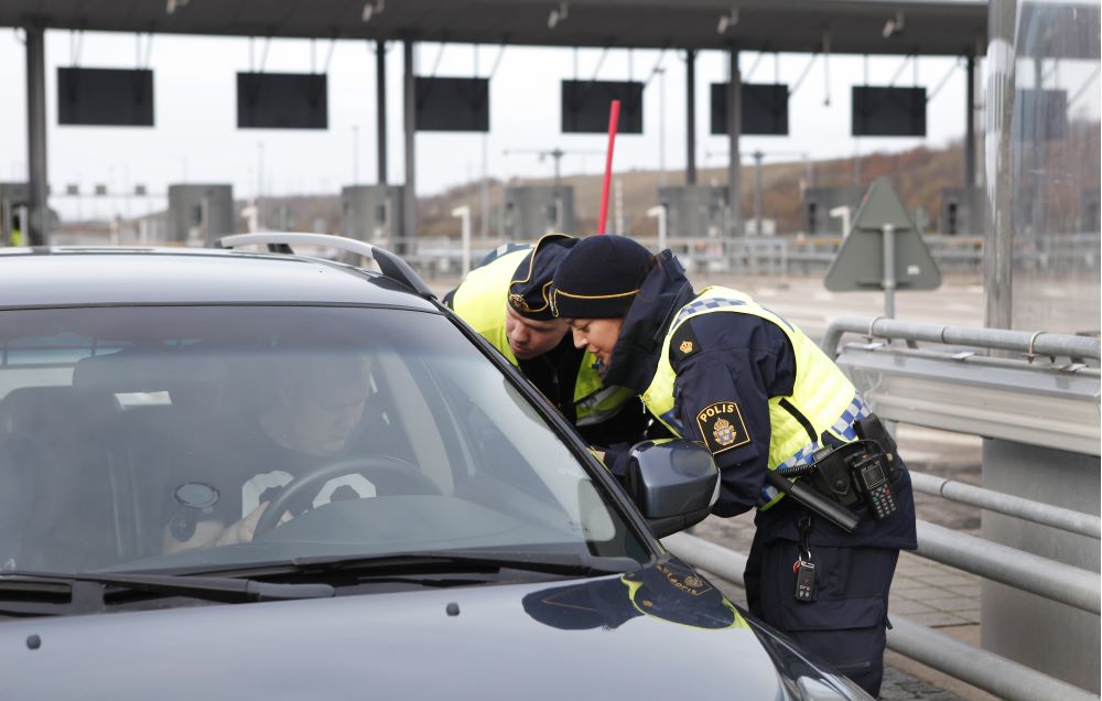 Två poliser i samtal med bilist. Bakgrund belatstationn vid gränsen.