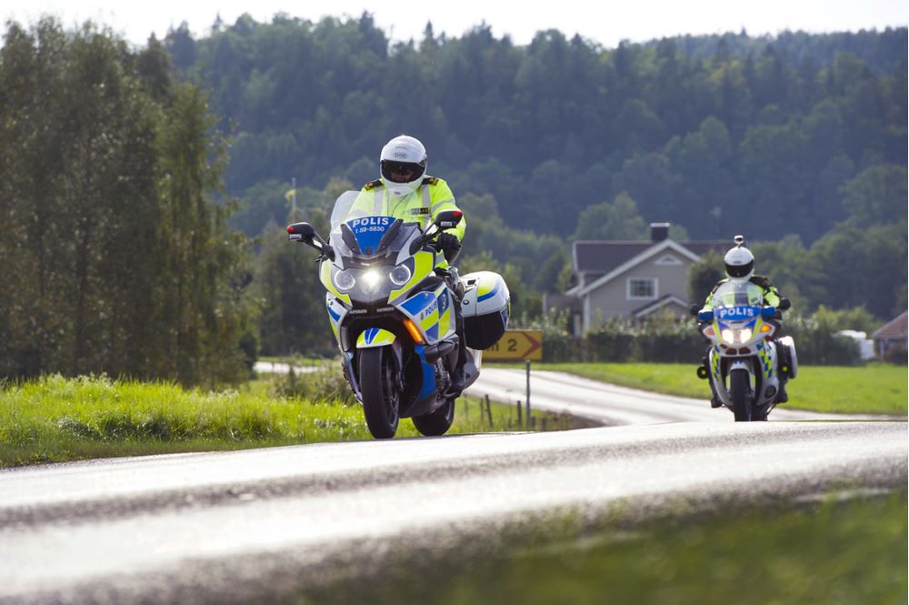 Två poliser som kör varsin polismotorcykel på en smal väg på landsbygden.