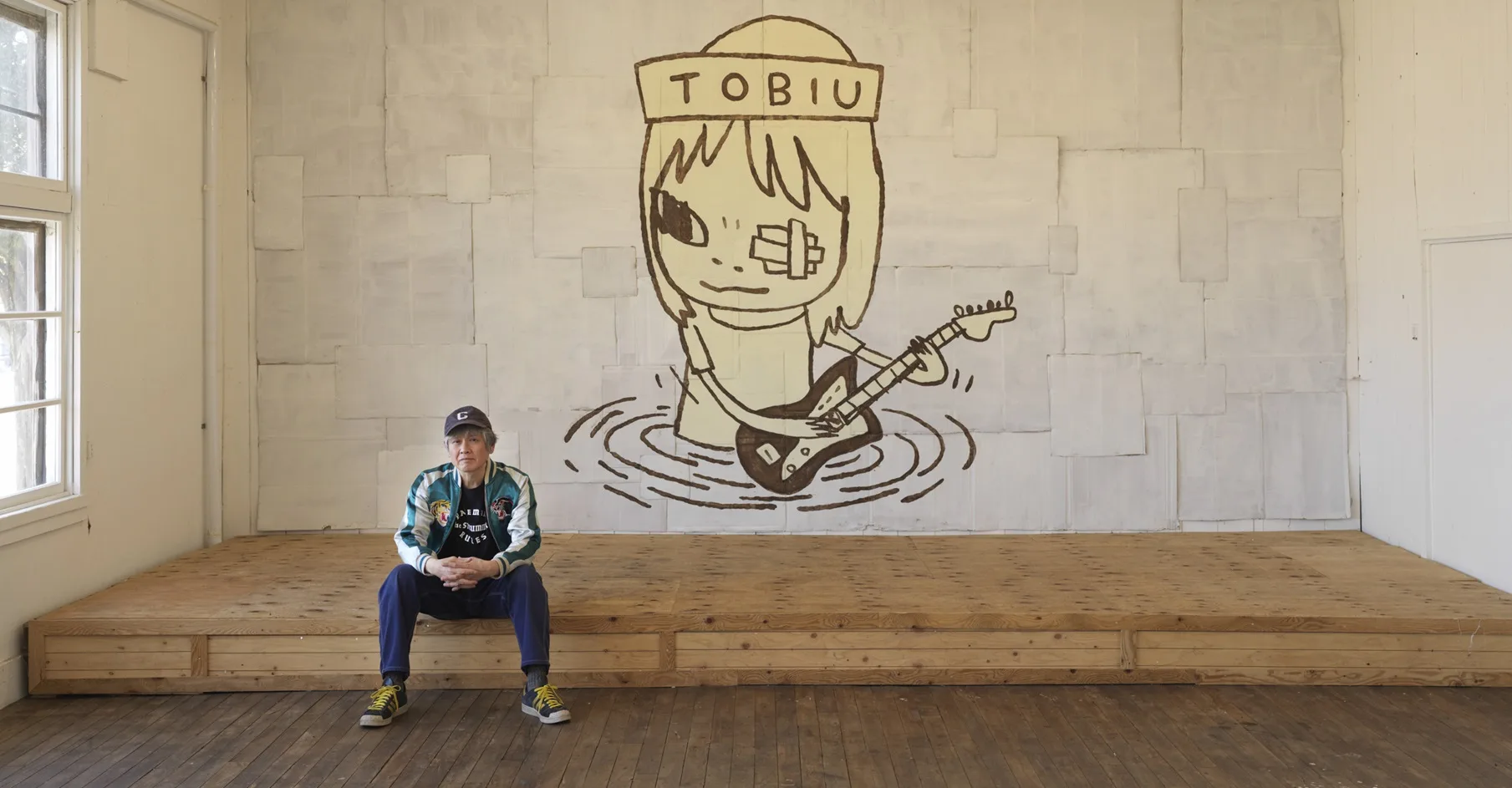 Yoshitomo Nara seated in front of TOBIU, 2019, donated by the artist to the TWO x TWO for AIDS and Art auction, 2021.