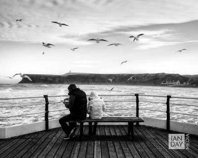 Seagulls hover overhead as people try eating fish and chips on Saltburn Pier.