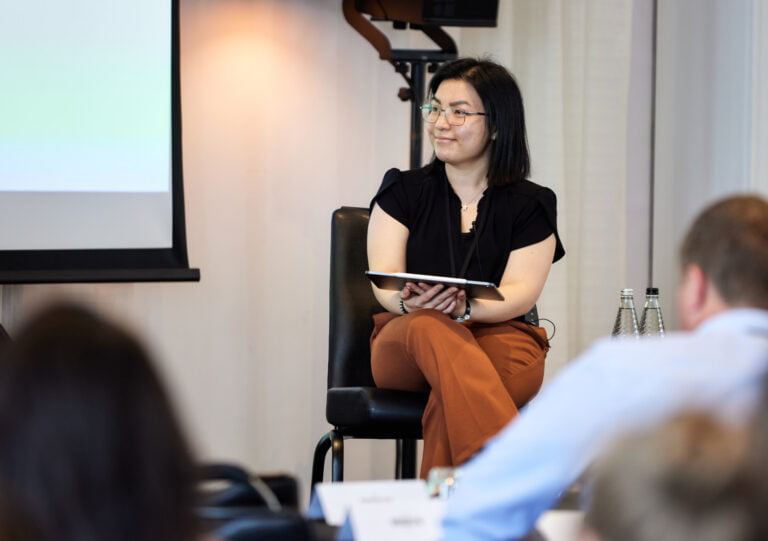 This is a photo of Nicole Lee, member of our advisory board. Nicole is a light-skin Asian lady, with short dark hair and glasses. In this photo, she is sitting on a char with her legs crossed, holding a tablet in her right hand. Nicole is wearing a black blouse and brown trousers. She is looking off camera, towards her right.