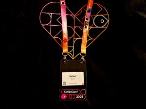 KotlinConf 2025 t-shirt with neon heart logo and the badge of Robert Wloch with collected pins on the band while diving into the Kotlin ecosystem