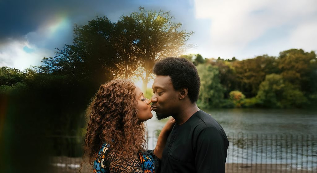 Couple embracing by serene water backdrop.