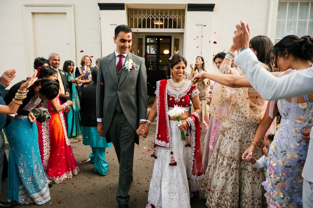 Newlywed Indian couple walking through a petal confetti tunnel outside the entrance of Sandwell Register Office in West Bromwich.