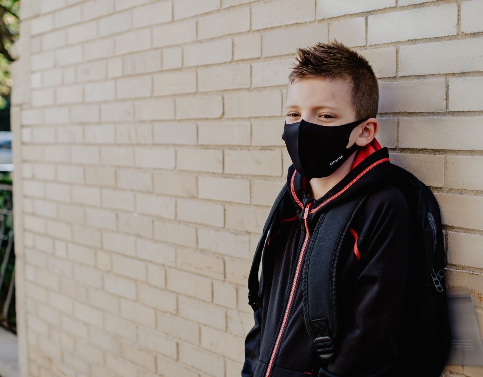 A young student leaning on a wall wearing a face mask a face and