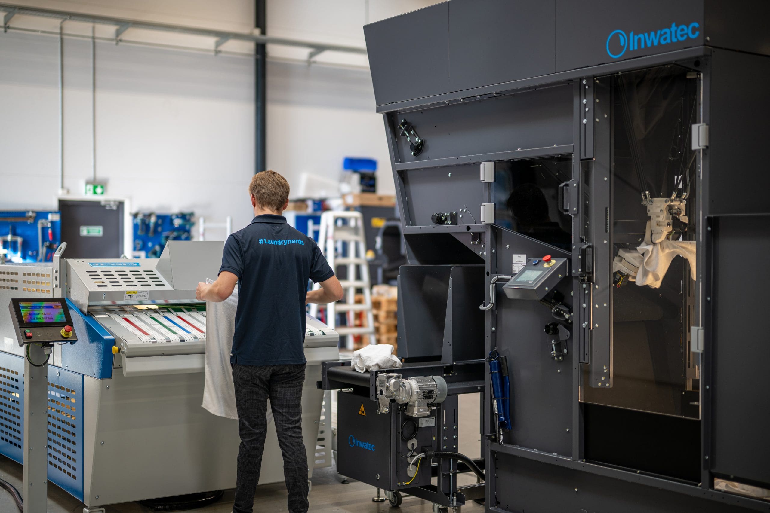 Inwatec employee with #laundrynerds on the back is showing how to feed towels into the Thor Towel Machine.