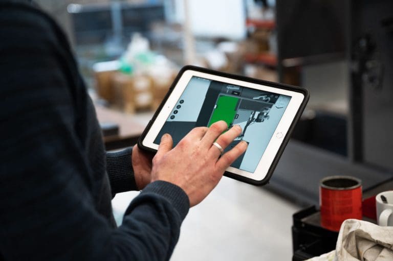 A man holding a tablet. On the screen the tablet is showing a 3D drawing of a machine.