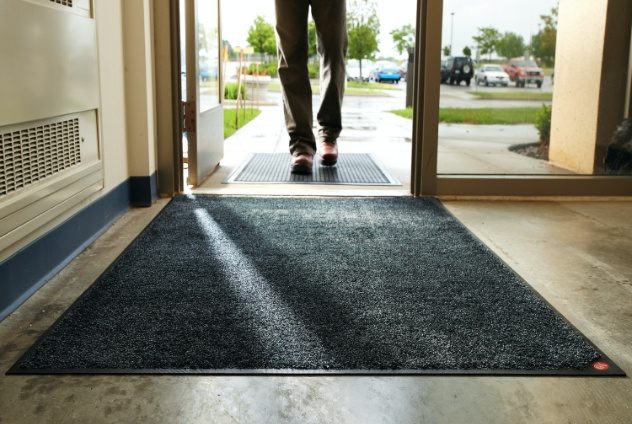 The entrance to a building where you see a clean mat laying inside the door.