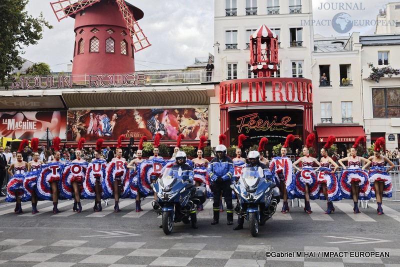 Les motards officiels du Tour de France prennent place devant les danseuses du Moulin Rouge formant l'inscription « TOUR DE FRANCE », place Blanche à Paris.