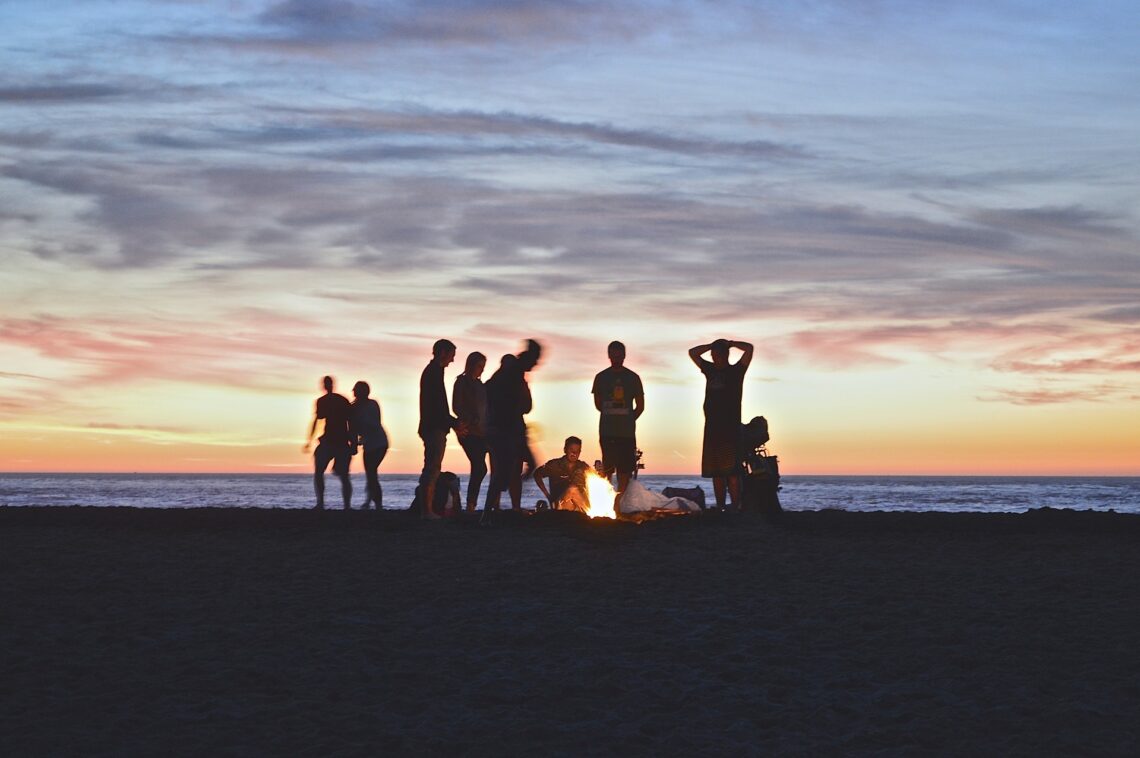 Small crowd at the beach with bonfire during sunset