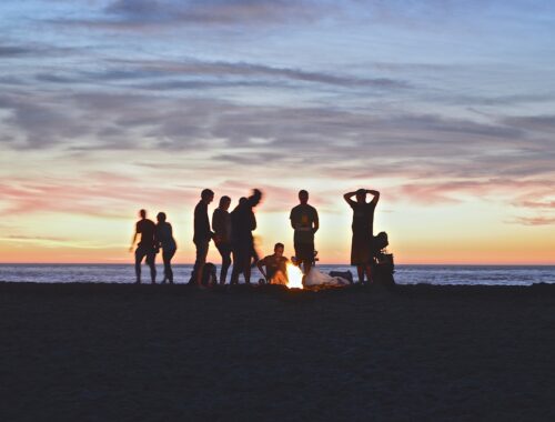 Small crowd at the beach with bonfire during sunset