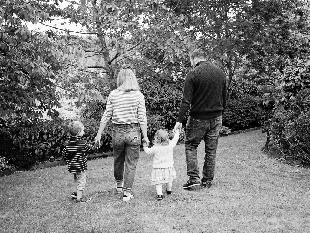 black and white photo of two kids and parents walking away holding hands - family photography edinburgh