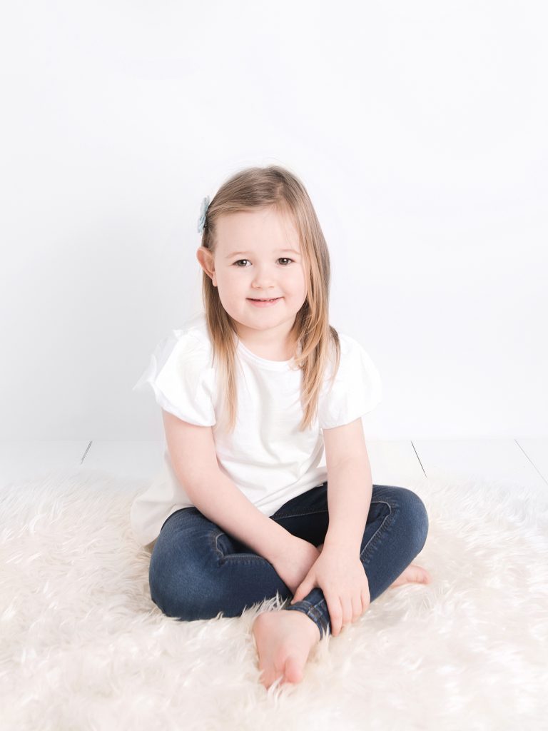 three year old girl sitting looking at camera, studio photography posing