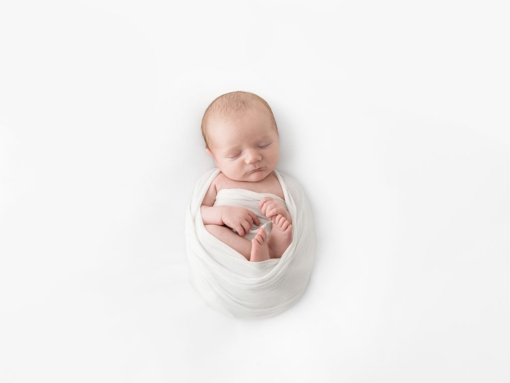 newborn on white posing wrapped on his back