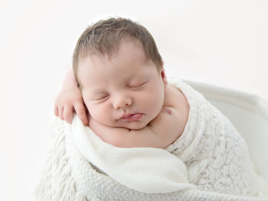 baby in a white basket posing on tummy