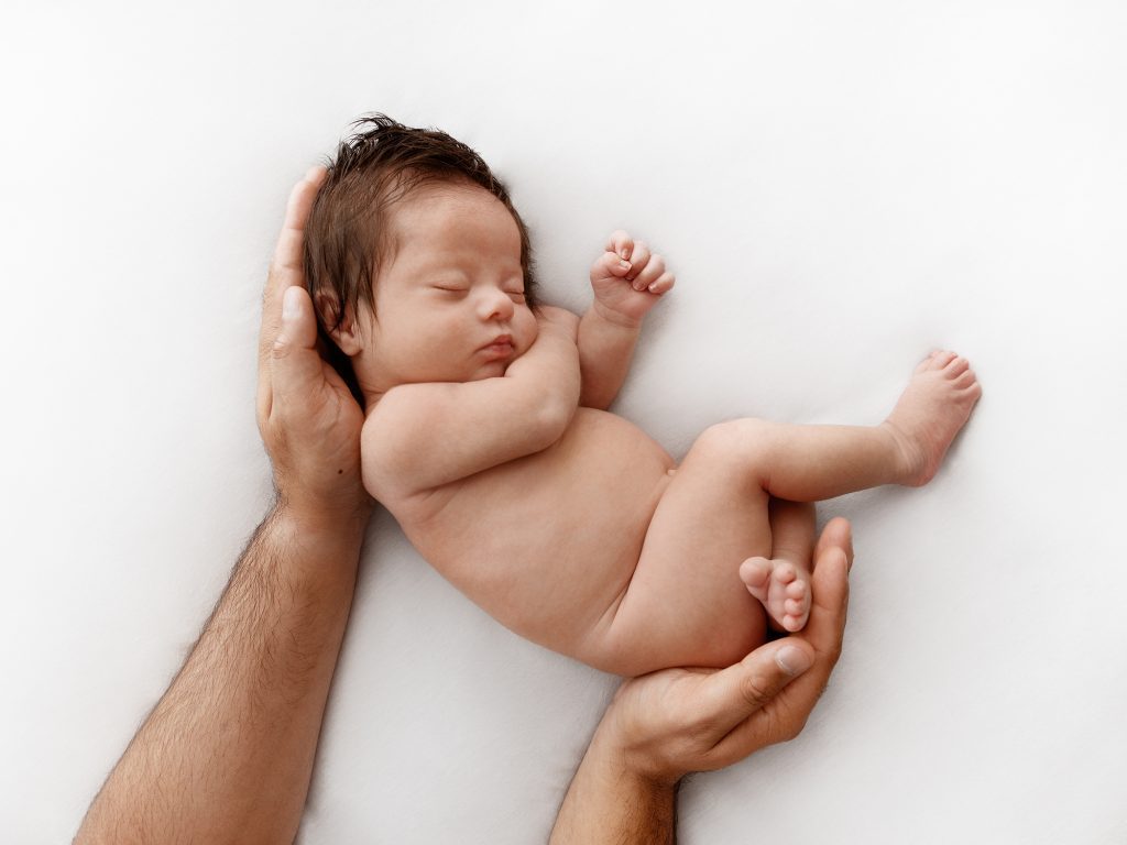 newborn with dads hands posing studio all white photography