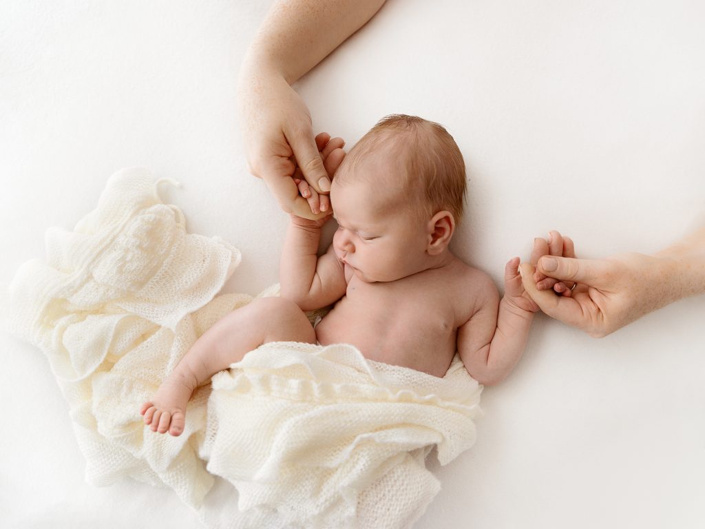 newborn posing with parents hands