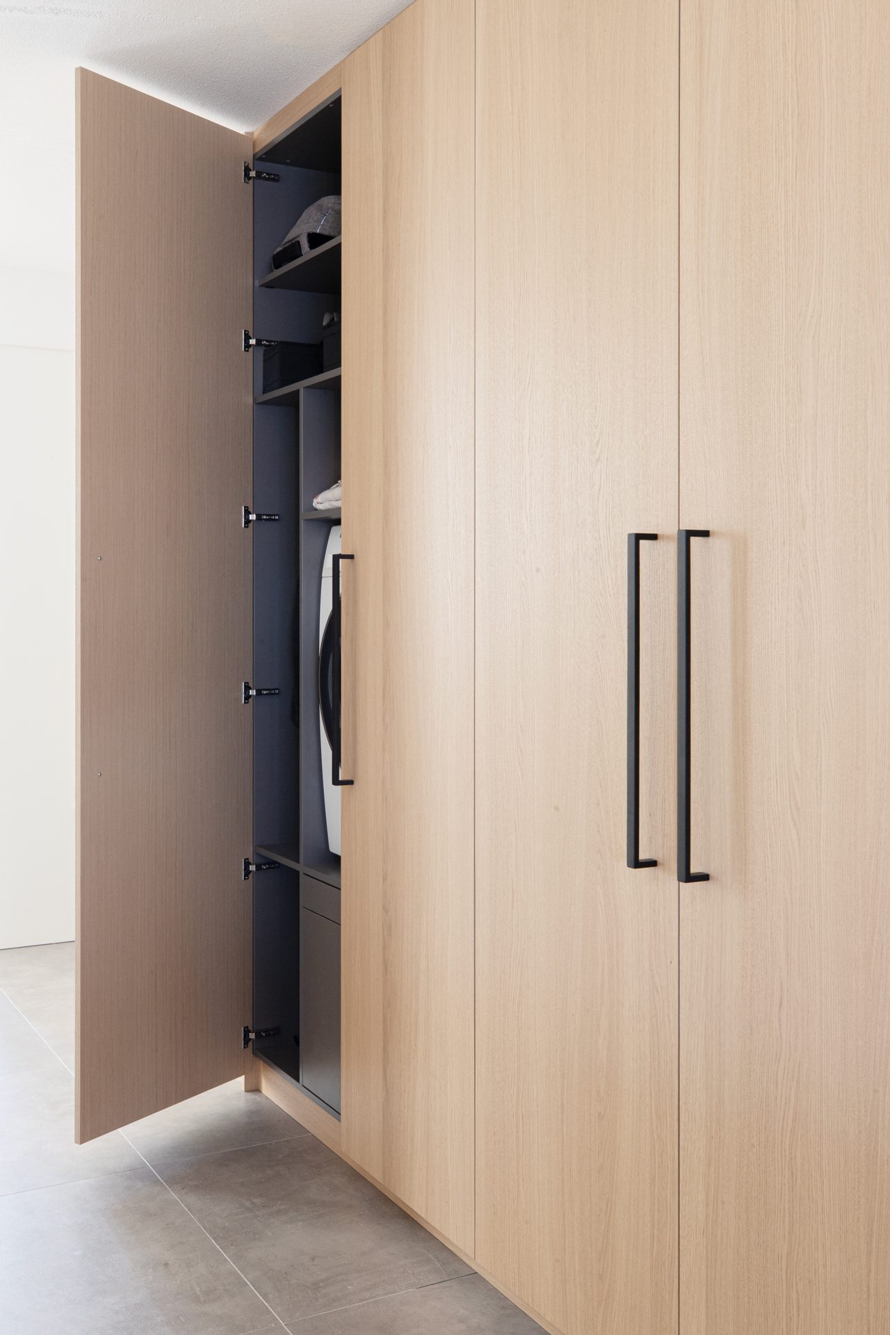 wasmachine-kast-op-maat-eiken-fineer-interieurbouw-amsterdam Kamerhoge kastenwand in eikenfineer met geïntegreerde wasmachine en stalen greep