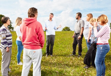 Carl plesner teaches NVC to a group of people standing in a circle in a field