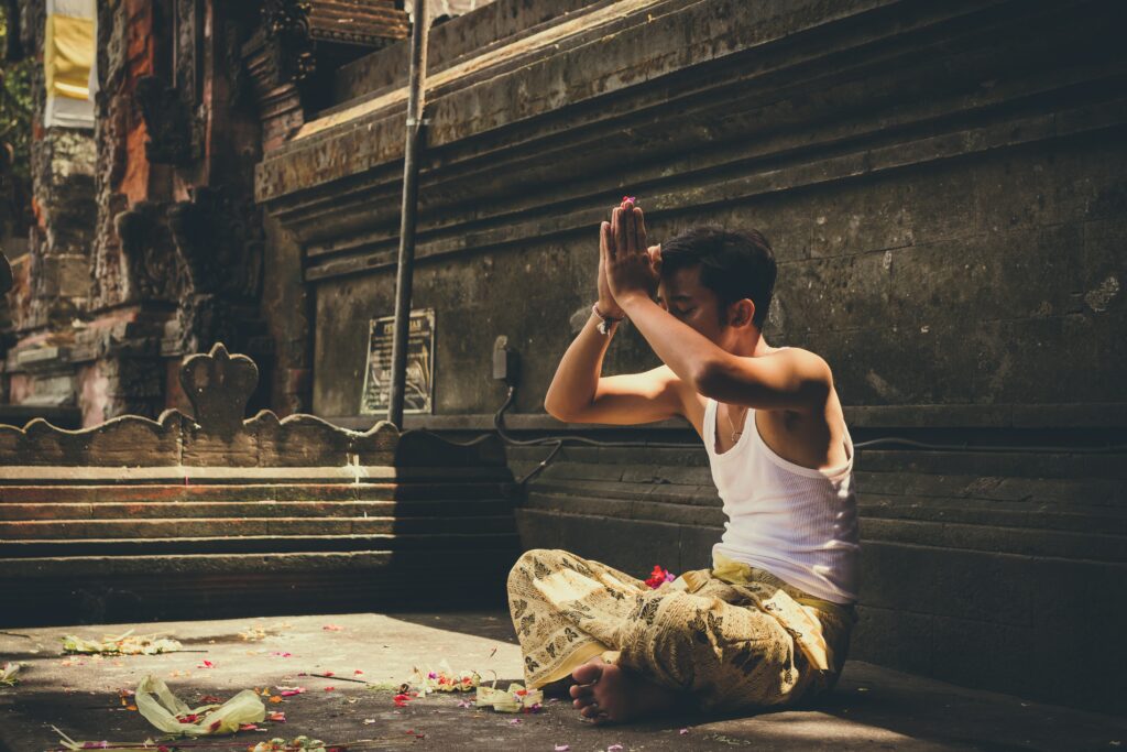 en religiøs mand sidder på jorden med krydsede ben og armene over hovedet, mens han beder en bøn