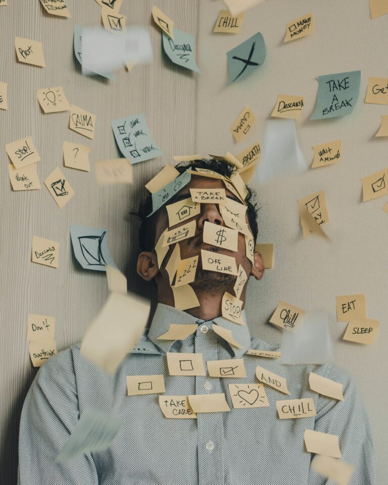 træt mand sidder med post-it noter klistret over hans ansigt, på noterne er der skrevet stressende faktorer