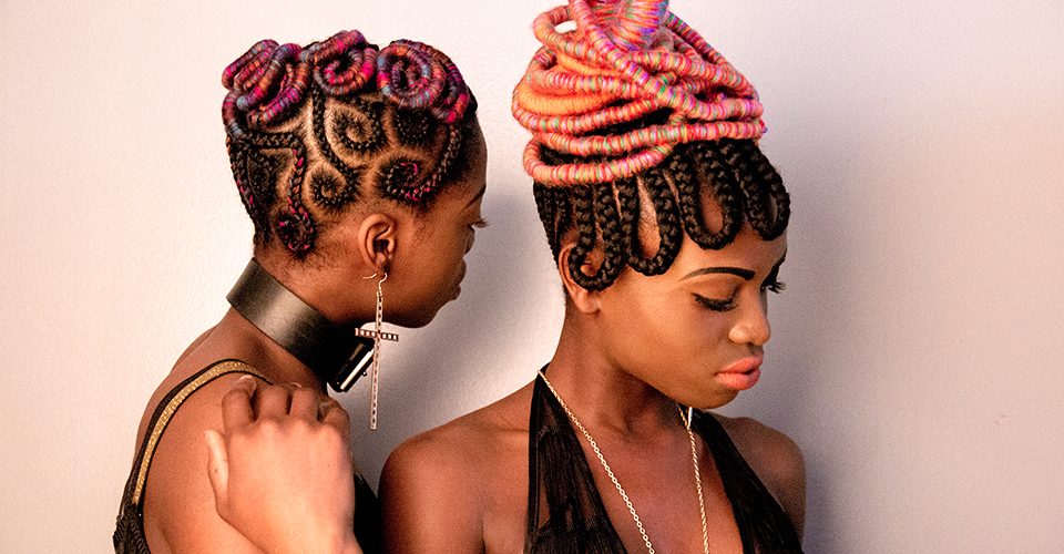 black and white photo of two black models in colorful intricate braids and vintage fashion