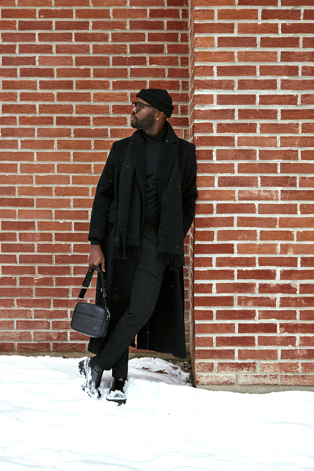 black male model in black winter coat against brick wall