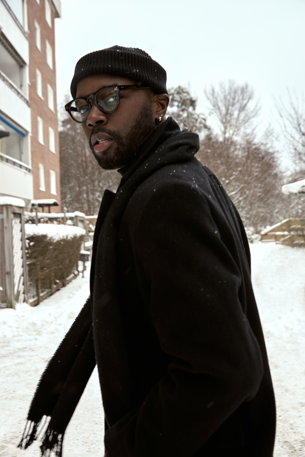 black man in snow wearing black glasses and black overcoat