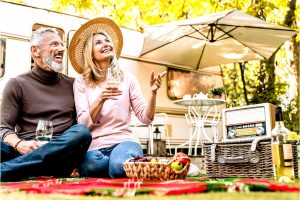 Koppel 60+ zit voor een caravan te picknicken met een glas wijn, genietend van hun leven