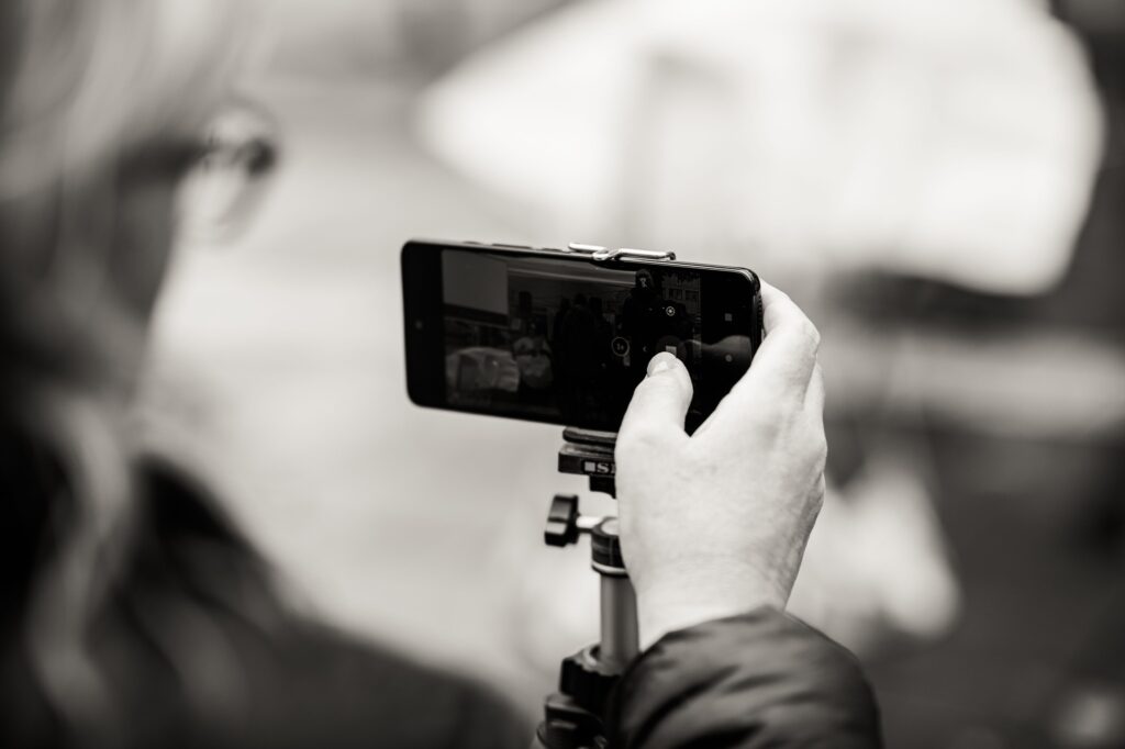 Svartvitt foto. Mobiltelefon på stativ för att filma. Ingelas ansikte och hand skymtas.