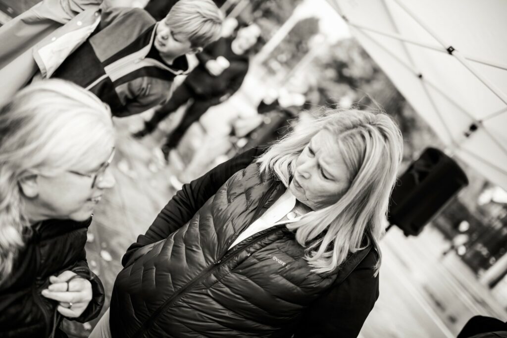 Svartvitt foto. Ingela och Anki, FQs styrelse diskuterar, i bakgrunden tältduk och människor som börjar samlas.