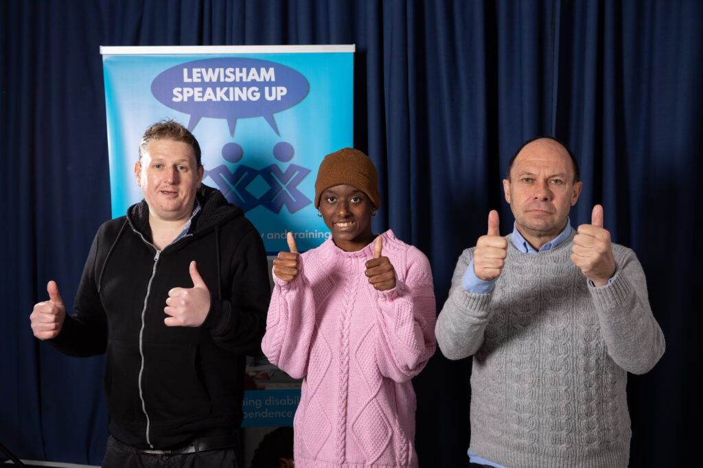three of lewisham speaking up's clients giving thumbs up to the camera; behind them is a sign with the LSU logo