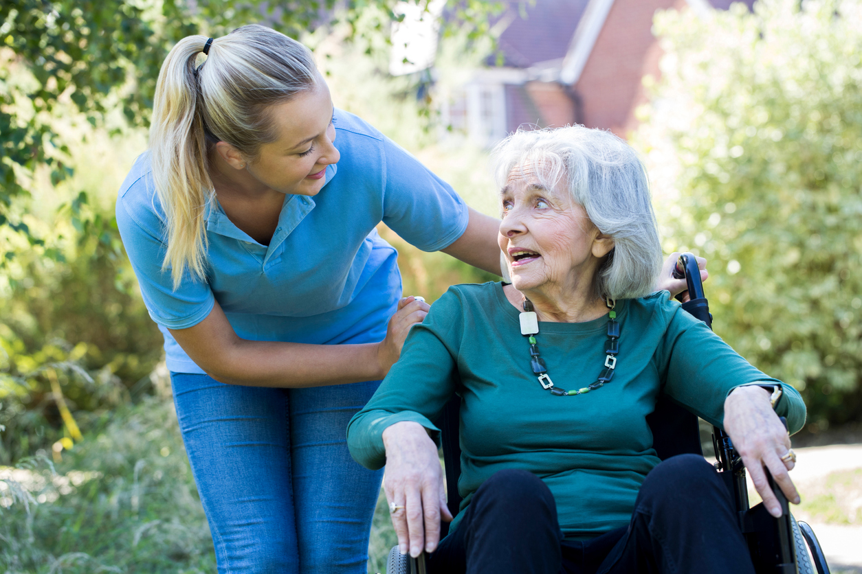 Carer Pushing Senior Woman In Wheelchair In Garden