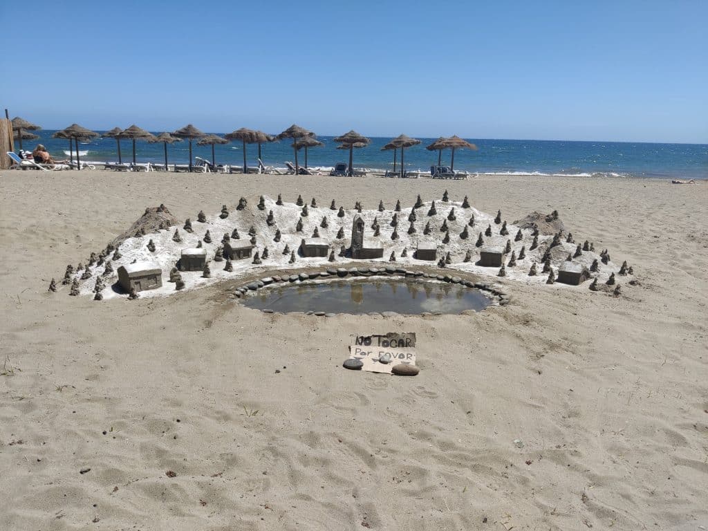 Fjell landskap med trær og hus laget av sand, på stranden. 