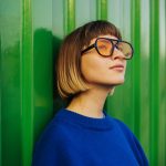 Female in blue shirt and sunglasses leaning against a green container