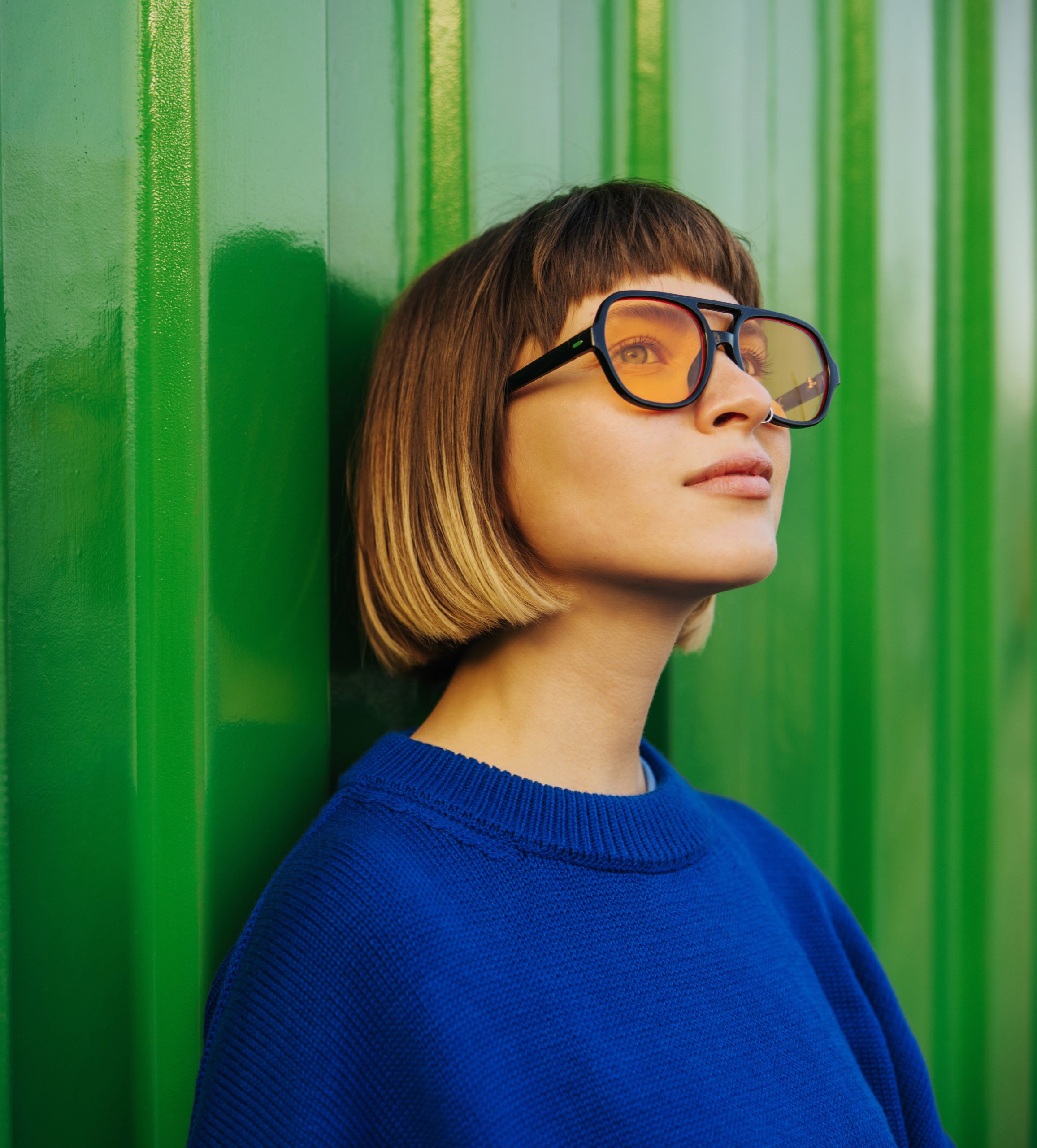 Female in blue shirt and sunglasses leaning against a green container