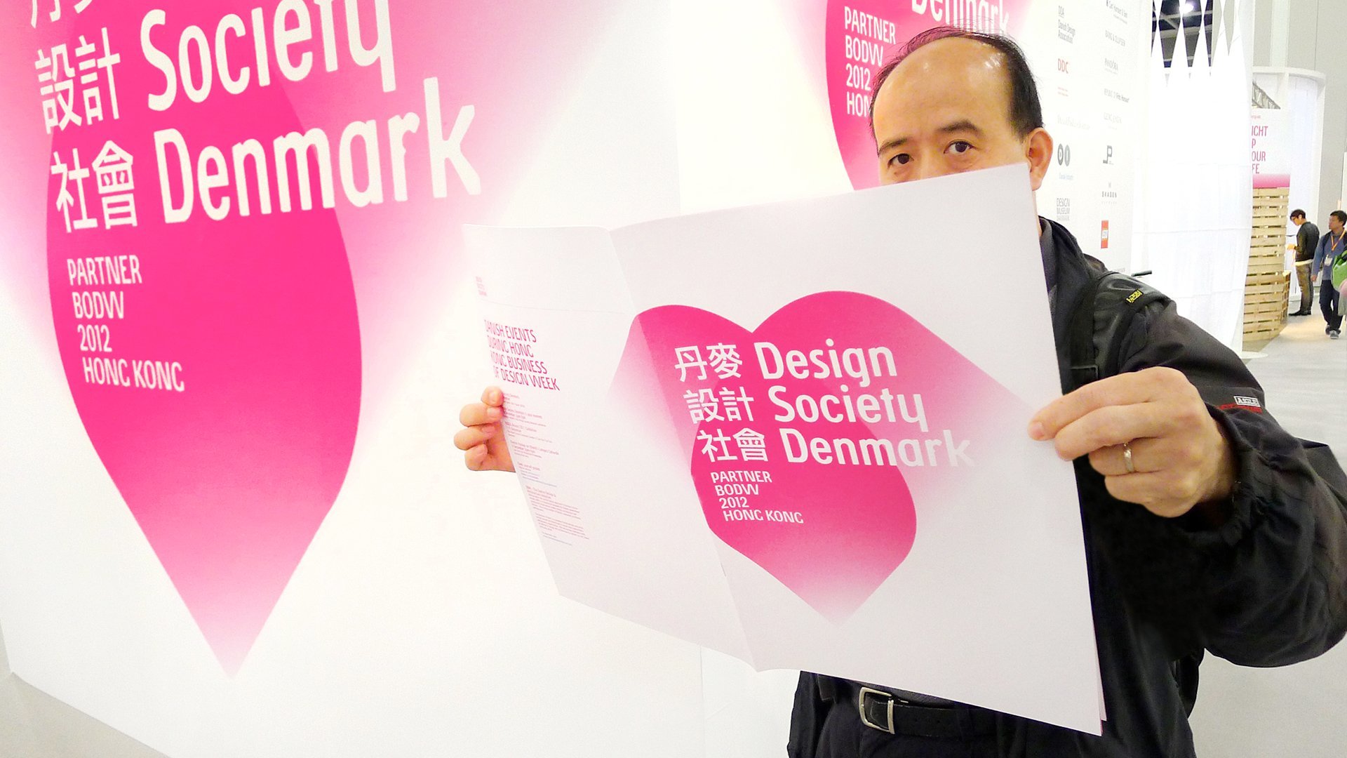 Image of visitor showcasing a Design Society Denmark catalogue by LOOP Associates at event.