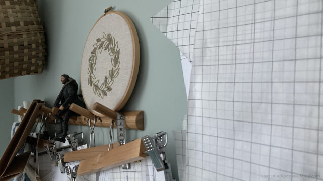 A photo of a wall in my sewing room, showing paper patterns on hangers, an embroidery of a simplified wreath, and a mini Aragorn action figure.