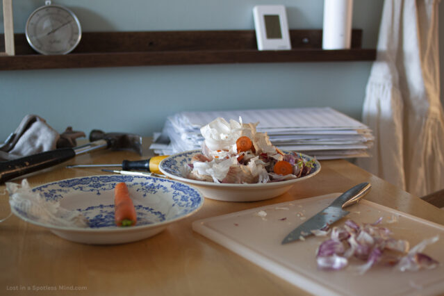 A photo of a messy kitchen table, with vegetable scraps, sheet music, and various tools.