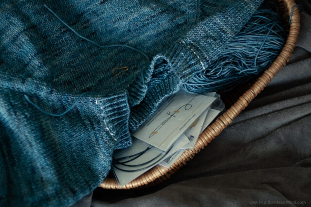 Close-up of a knitted sweater-in-the-making, on top of a basket of knitting tools.