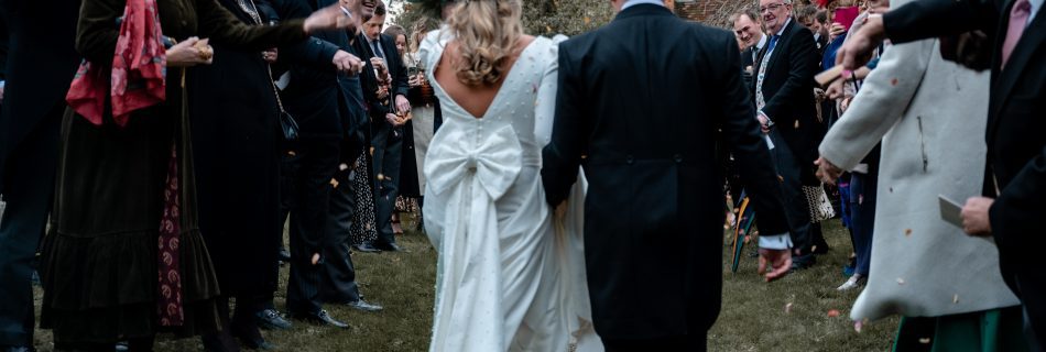 A bride and groom walking away through confetti
