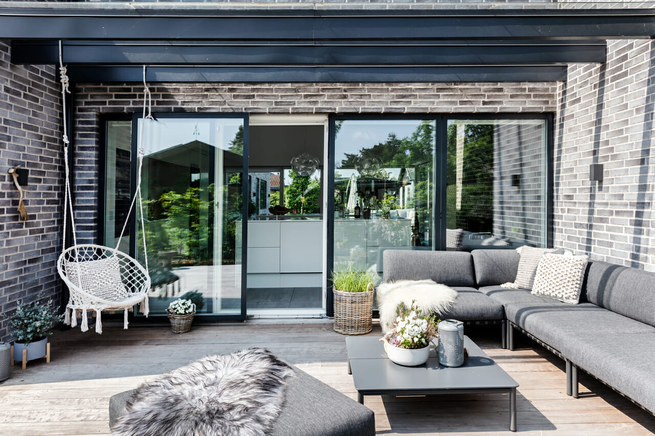 Terrasse med loungeområde, hængestol og direkte indgang til køkken-alrum, nybygget funkisvilla