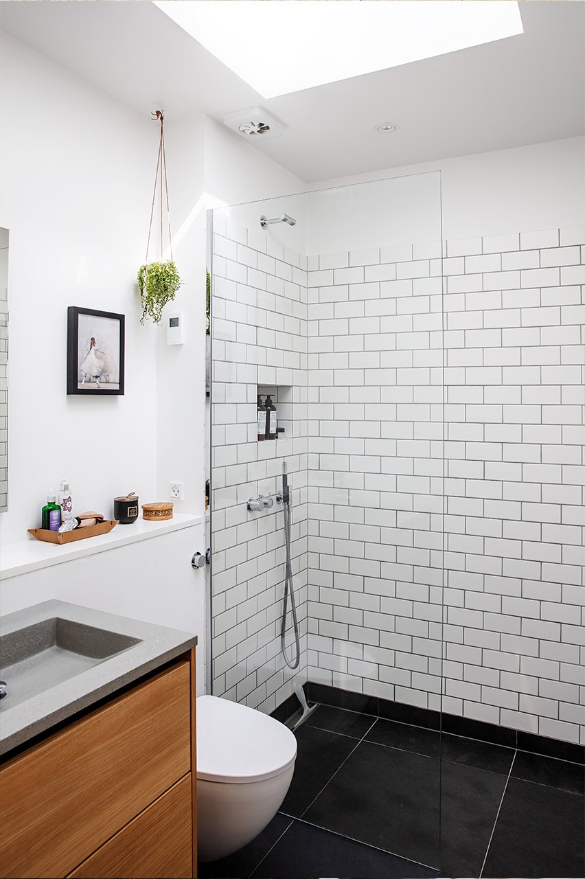 Totalrenoveret badeværelse med ovenlysvindue, metrofliser på væg og sorte klinker på gulv