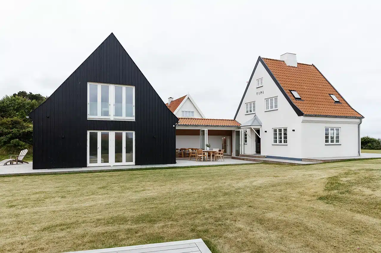 Bevaringsværdigt sommerhus med tilbygning blev totalrenoveret, hvidt Bedre Byggeskik-hus og sort tilbygning.