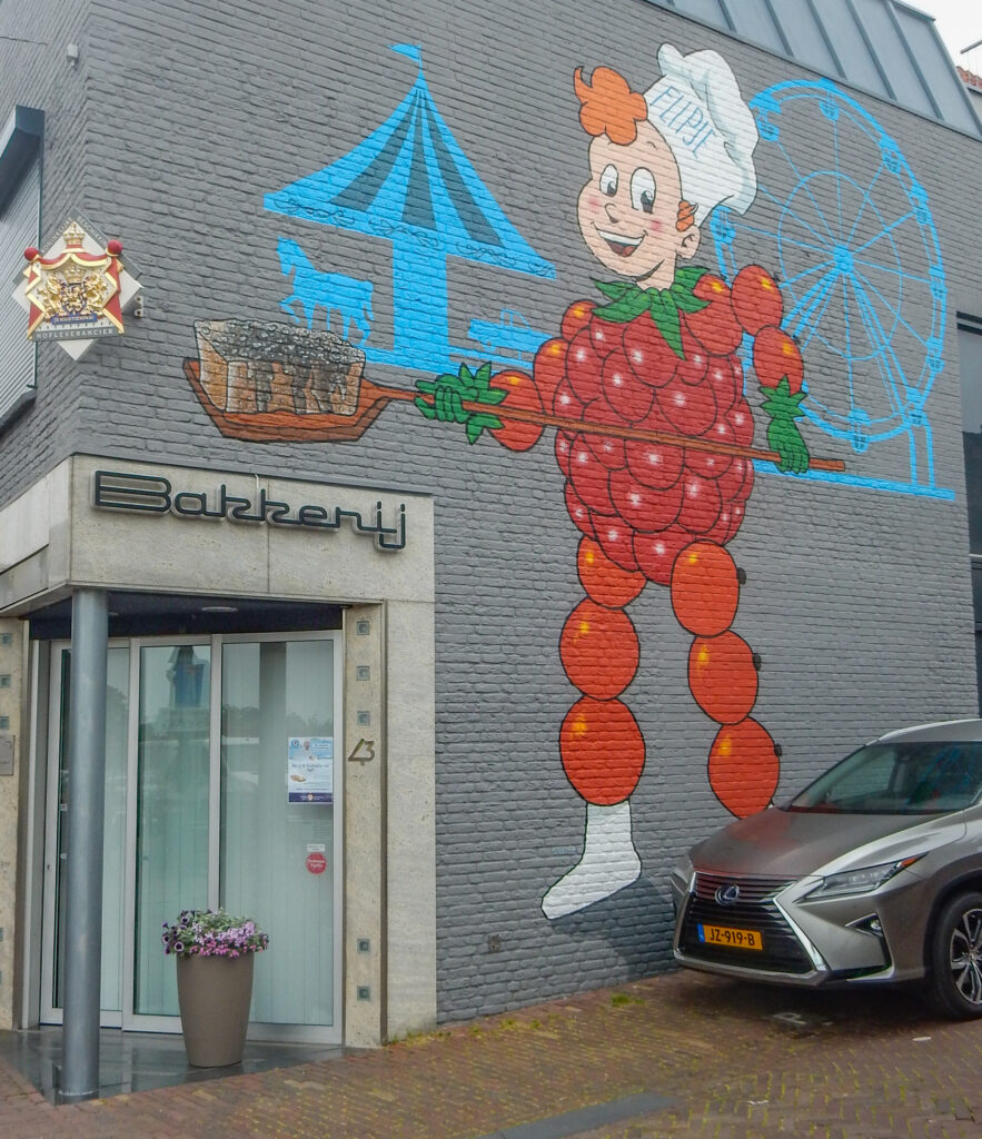 Flipje ontstond als reclamefiguurtje van jamfabriek ‘De Betuwe’ in Tiel. Achter Flipje een silhouet van de Kermis. In zijn handen zien we een bakkersgereedschap dat wordt gebruikt om de beroemde Kermiskoek in of uit de hete oven te zetten. De cake zelf heeft een beetje licht effect in de verf.