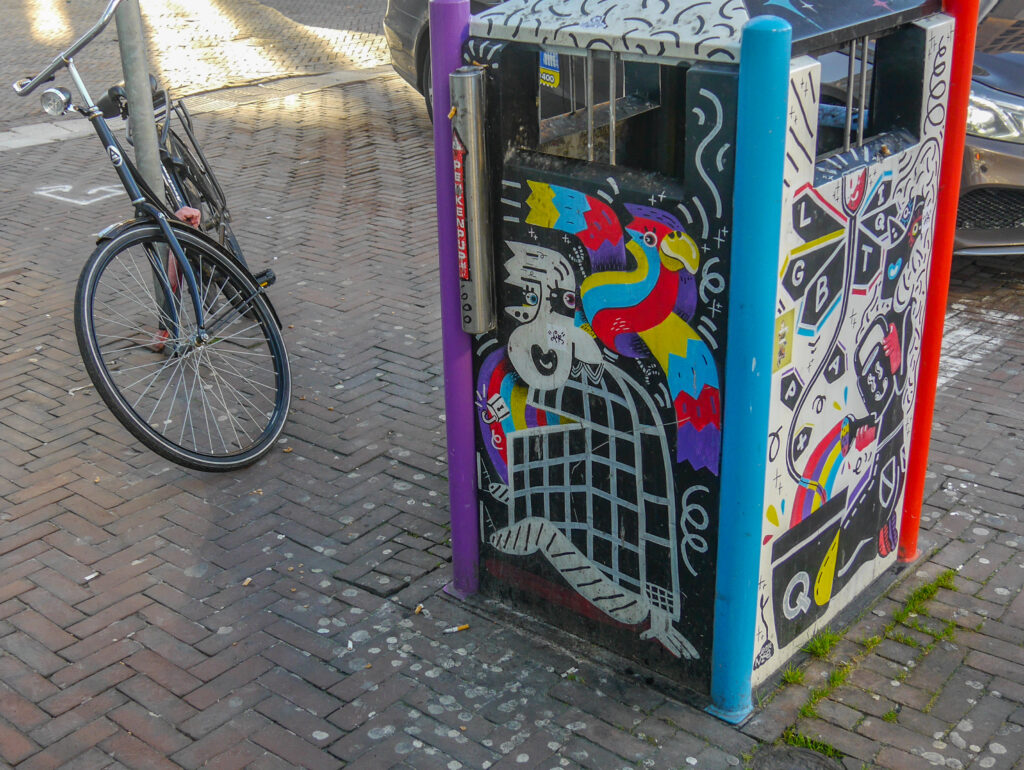 Van lelijke, vieze vuilnisbak naar kleurrijk graffitikunstwerk en omdat die vlakbij de regenboog-zebrapad staat, heeft die een LHBT-thema gekregen.